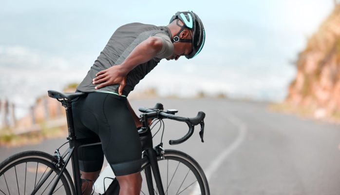 Cyclist holding their lower back beside a road bike, representing care for sports-related back pain and recovery