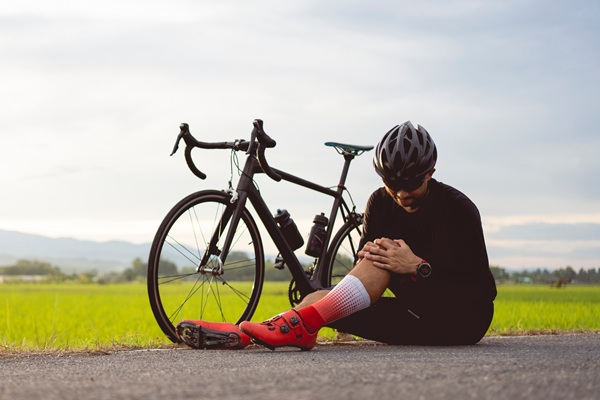 Cyclist sitting beside a road bike holding their knee, representing treatment for sports injuries, knee pain, and recovery